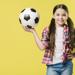Girl holding soccer ball in front of yellow background