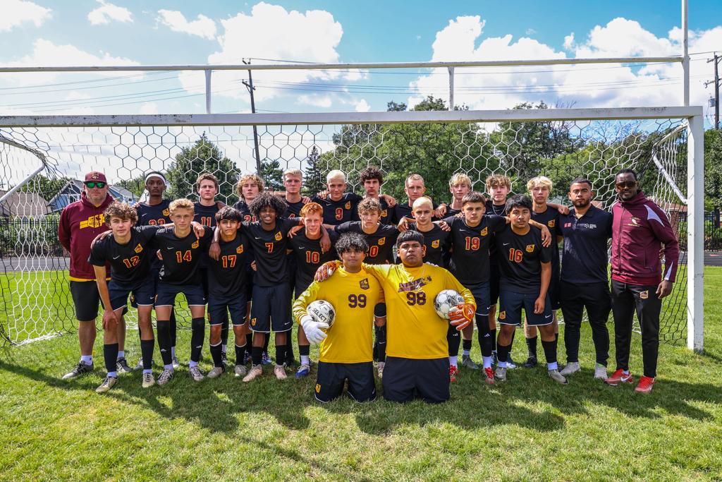 Image of Minneapolis Roosevelt High School’s boys varsity soccer team of 2023 grouped together with their coach for a team photo on the field at Al Gowans Stadium.
