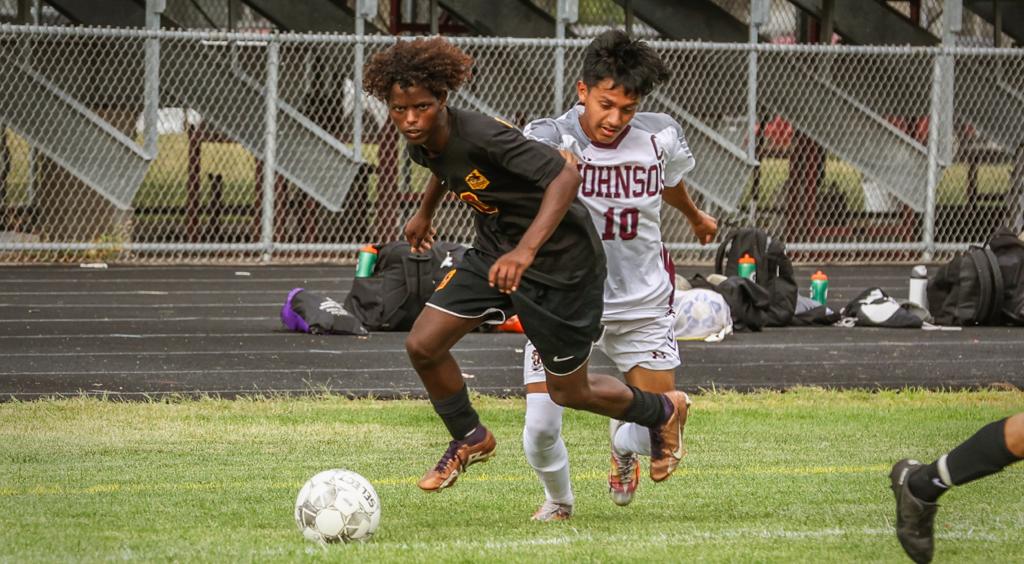 Image of Minneapolis Roosevelt High School Boys varsity soccer player looking upfield as he dribbles past a midfield opponent during a game at Al Gowan’s stadium.