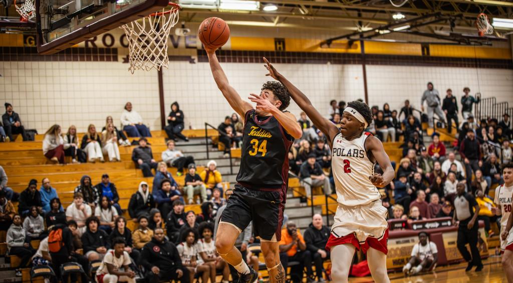Image of Minneapolis Roosevelt High School basketball boys player driving to the basketball for a layup, his arm extended and hand cupping the ball with the defender inches behind, his arm over the top of his head