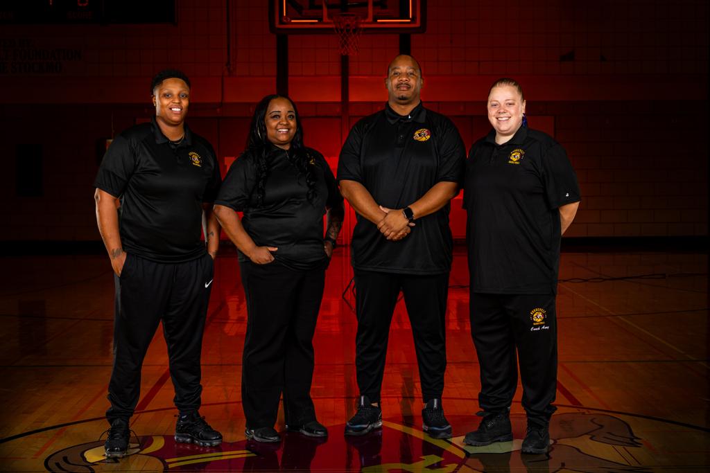 Minneapolis Roosevelt Girls Basketball Coaching Staff pose in a dimly lit Jack Wells Gymnasium